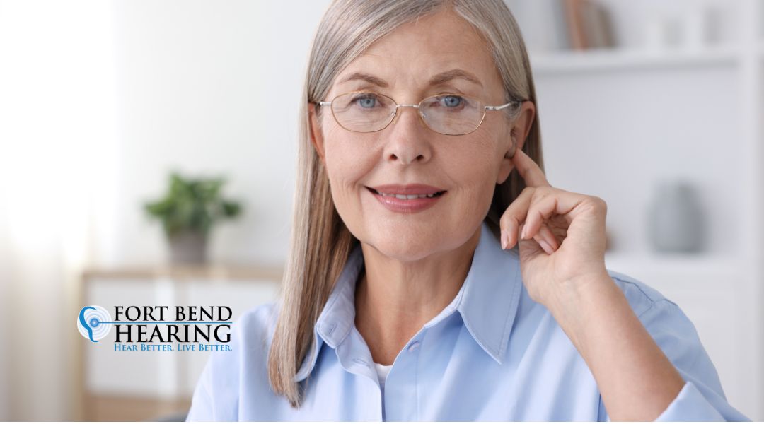 Woman touching her hearing aid, representing AI hearing aid features at Fort Bend Hearing